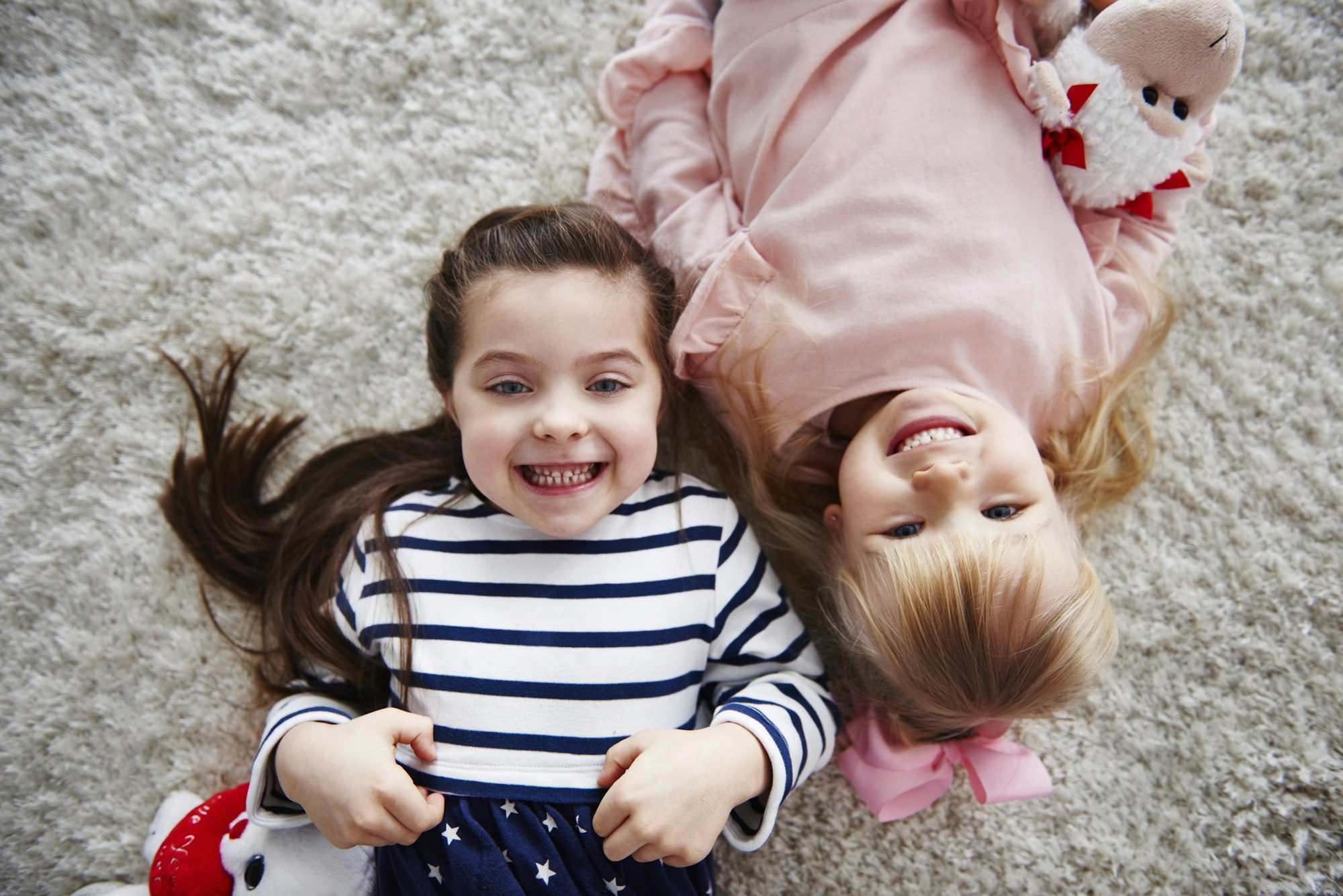 Portrait of two grinning little sisters lying on the carpet